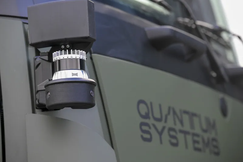 Abgebildet ist ein an der Kabine eines olivgrünen Fahrzeugs montiertes Sensorsystem zur Umfelderfassung. Auf der Fahrzeugtür ist der Schriftzug eines Technologieunternehmens zu sehen.