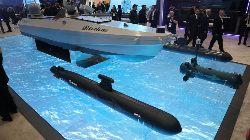 Am Stand des türkischen Rüstungsunternehmens ASELSAN werden Modelle unbemannter maritimer Systeme präsentiert: das unbemannte Überwasserfahrzeug „TUFAN" sowie mehrere autonome Unterwasserfahrzeuge der Baureihe „KILIÇ" in verschiedenen Größen, ausgestellt auf einer beleuchteten Wassersimulationsfläche vor Messepublikum.