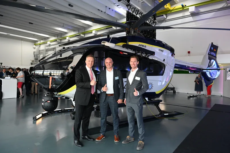 Drei Männer posieren in einer Halle vor einem Hubschrauber des Typs Airbus H145 der bayerischen Polizei. Das Luftfahrzeug trägt das Kennzeichen D-HPBA.