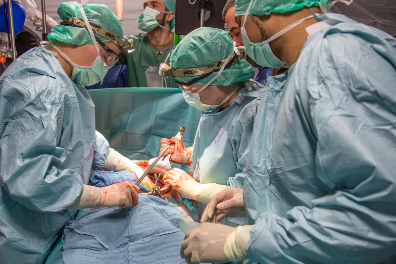 Ein medizinisches Team führt im Rahmen der Übung "Medical Quadriga 2026" unter sterilen Bedingungen eine chirurgische Operation durch. Die Chirurgen und Assistenten tragen OP-Kleidung sowie Stirnlampen, während sie mit medizinischen Instrumenten am Patienten arbeiten.
