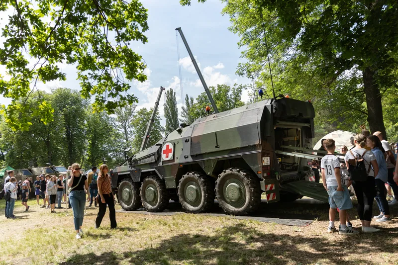 Ein schweres geschütztes Sanitätskraftfahrzeug des Typs GTK Boxer der Bundeswehr wird im Rahmen einer öffentlichen Präsentation von Besuchern besichtigt. Das gepanzerte Radfahrzeug ist mit geöffnetem Heck und ausgefahrener Trageplattform auf einer Rasenfläche ausgestellt.