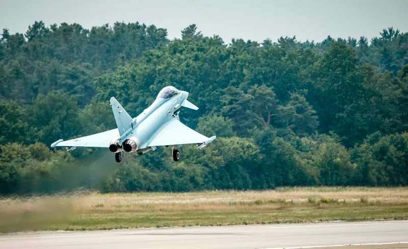 Eurofighter der Luftwaffe hebt mit ausgefahrenem Fahrwerk von einer Startbahn vor einer Waldkulisse ab