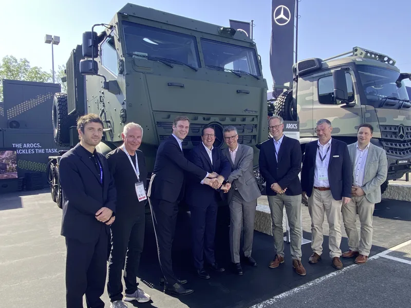 Männer beim Handschlag vor zwei Mercedes-Benz Arocs Militär-Lkw auf einer Fachmesse für Wehrtechnik