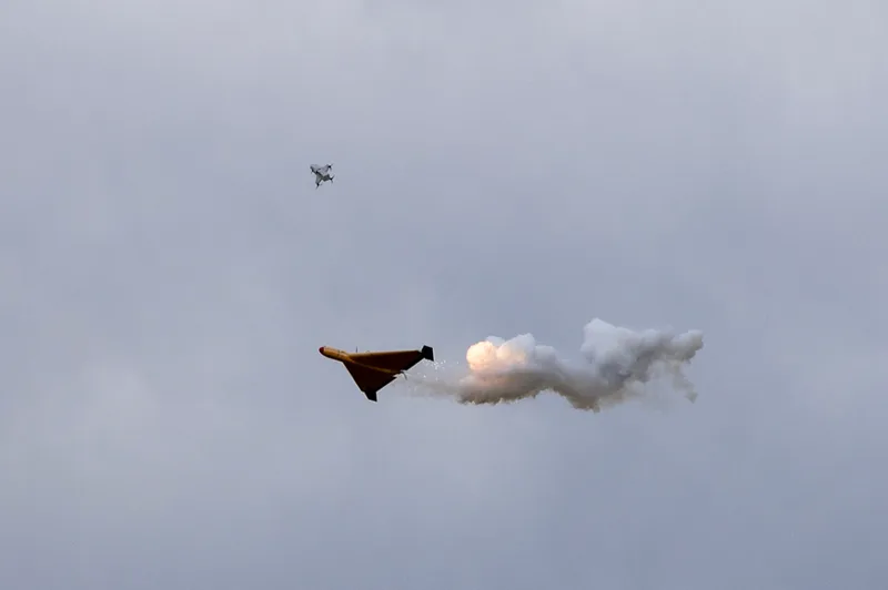Gelbe Zieldarstellungsdrohne mit Rauchspur am bewölkten Himmel vor einem Kampfflugzeug bei den DefenceTech Days