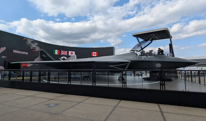 Modell des GCAP-Kampfflugzeugs auf einer Messe vor einer Displaywand mit den Flaggen von Italien, Großbritannien, Japan und Kanada