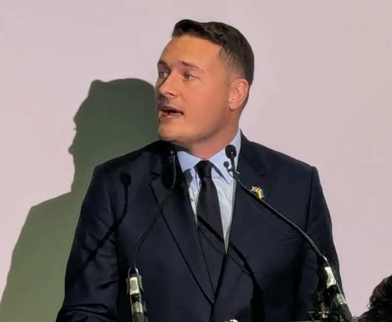 Wes Streeting hält an einem Rednerpult mit Mikrofonen eine Rede vor einem Logo des Rüstungsunternehmens BAE Systems