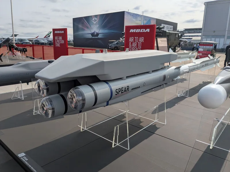 Vier MBDA SPEAR Lenkflugkörper an einem Mehrfach-Trägersystem auf einer Rüstungsmesse vor Informationswänden