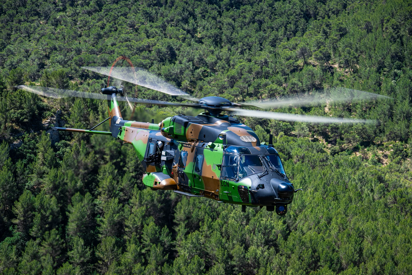 Ein Transporthubschrauber des Typs NH90 fliegt im Tiefflug über ein dicht bewaldetes Gebiet.