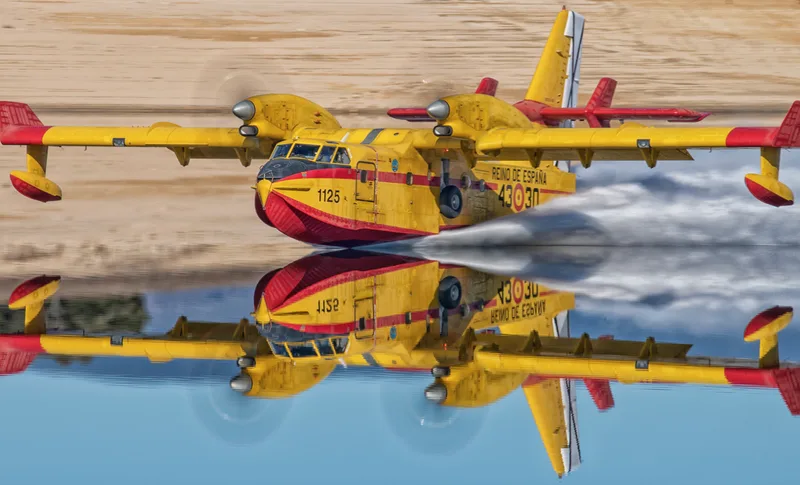Gelb-rotes Löschflugzeug Canadair CL-215T der spanischen Luftstreitkräfte bei der Wasseraufnahme auf einem Gewässer