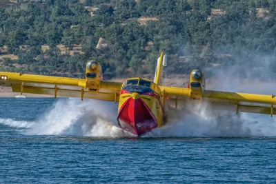 Ein Amphibien-Löschflugzeug des Typs Canadair CL-415 nimmt beim Scooping im Gleitflug Wasser von der Oberfläche eines Gewässers auf.