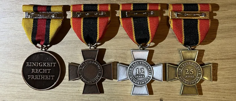 Ehrenmedaille und Ehrenkreuze der Bundeswehr in Bronze, Silber und Gold liegen nebeneinander auf einer Holzoberfläche
