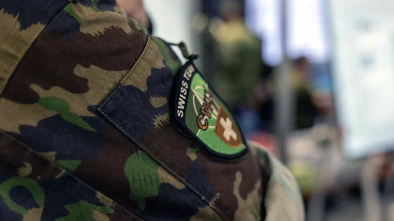 Angehöriger der Schweizer Armee mit CWIX-Ärmelabzeichen auf der Tarnuniform vor einem Arbeitsplatz mit Bildschirmen
