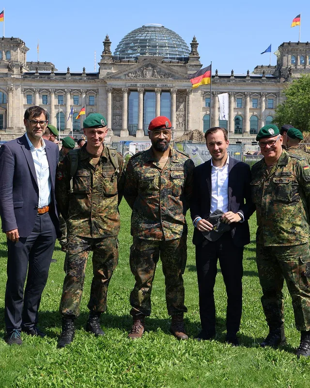 Drei Bundeswehrsoldaten in Flecktarn und zwei Zivilisten im Anzug vor dem Reichstagsgebäude in Berlin mit gelber Solidaritätsschleife