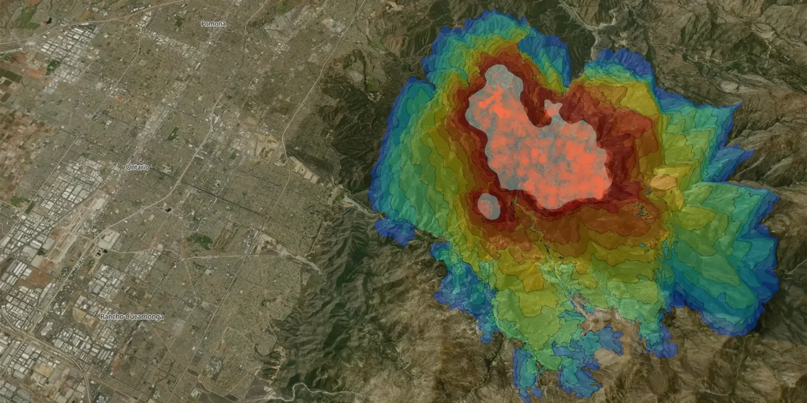 Eine satellitengestützte Geländekarte zeigt die digitale Simulation der Ausbreitung eines Waldbrandes in einer Gebirgsregion östlich von Los Angeles. Die farbigen, konzentrischen Linien markieren die zeitliche Entwicklung des Feuers nahe den US-amerikanischen Städten Pomona, Ontario und Rancho Cucamonga.