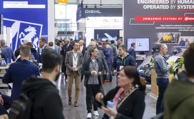 Fachbesucher auf der Messe XPONENTIAL Europe für unbemannte Systeme und Robotik. Im Hintergrund sind unter anderem die Ausstellungsstände der Hersteller Diehl Defence und Autel sowie ein Informationsstand des Landes Nordrhein-Westfalen zu sehen.