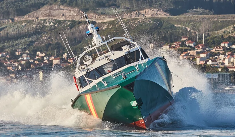 Grün lackiertes AISTER-Abfangboot der spanischen Guardia Civil bei hoher Geschwindigkeit vor einer hügeligen Küstenlandschaft