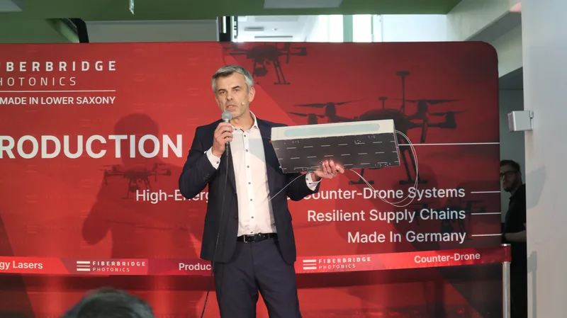 Repräsentant präsentiert eine optische Komponente von Fiberbridge Photonics vor einer Informationswand zu Laser- und Drohnenabwehr