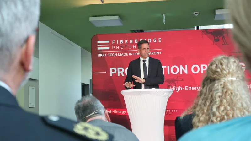 Redner spricht an einem Stehtisch vor einem Fiberbridge-Photonics-Banner bei einer Standorteröffnung vor Fachpublikum
