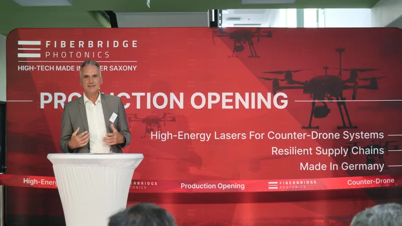 Redner an einem Stehpult bei der Produktionseröffnung von Fiberbridge Photonics vor einem Banner zur Hochenergielaser-Drohnenabwehr