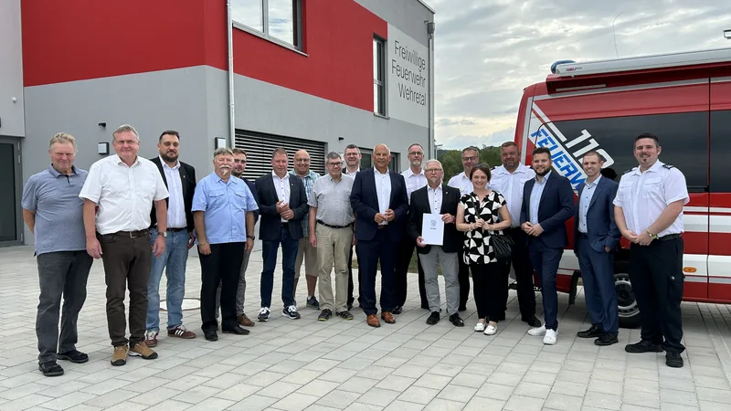 Übergabe eines Förderbescheids des Landes Hessen vor dem Gebäude der Freiwilligen Feuerwehr Wehretal mit rotem Einsatzfahrzeug