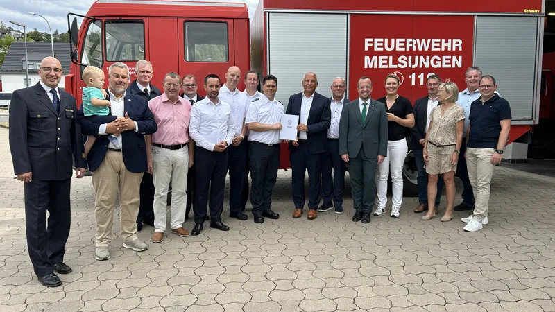 Vertreter aus Politik und Feuerwehr bei der Übergabe eines Förderbescheids vor einem Löschfahrzeug der Feuerwehr Melsungen mit Schmitz-Aufbau