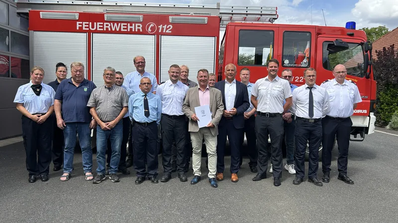 Feuerwehrleute und Politiker posieren vor einem Magirus-Löschfahrzeug bei der Übergabe eines Förderbescheids in Calden, Hessen