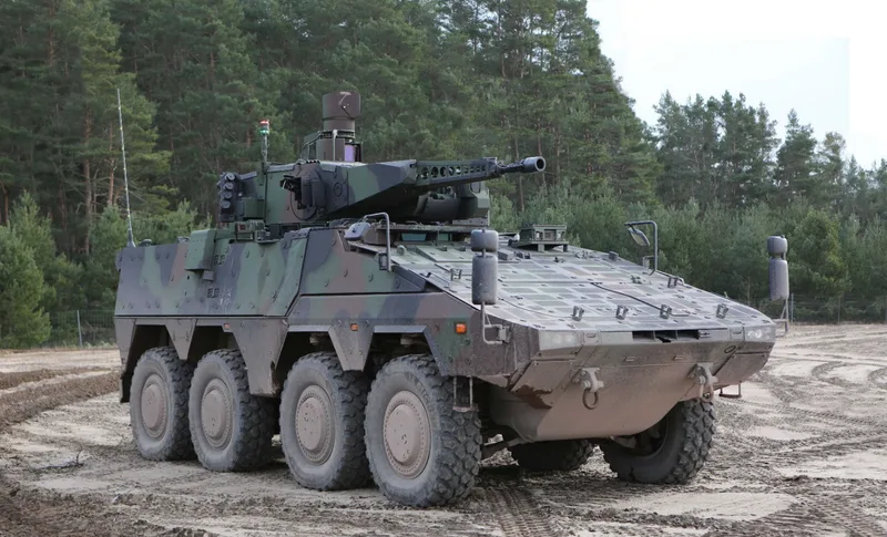 Gepanzertes Radfahrzeug GTK Boxer mit RCT 30-Turm und 30-mm-Maschinenkanone im Flecktarn auf einem sandigen Übungsgelände vor Waldkulisse