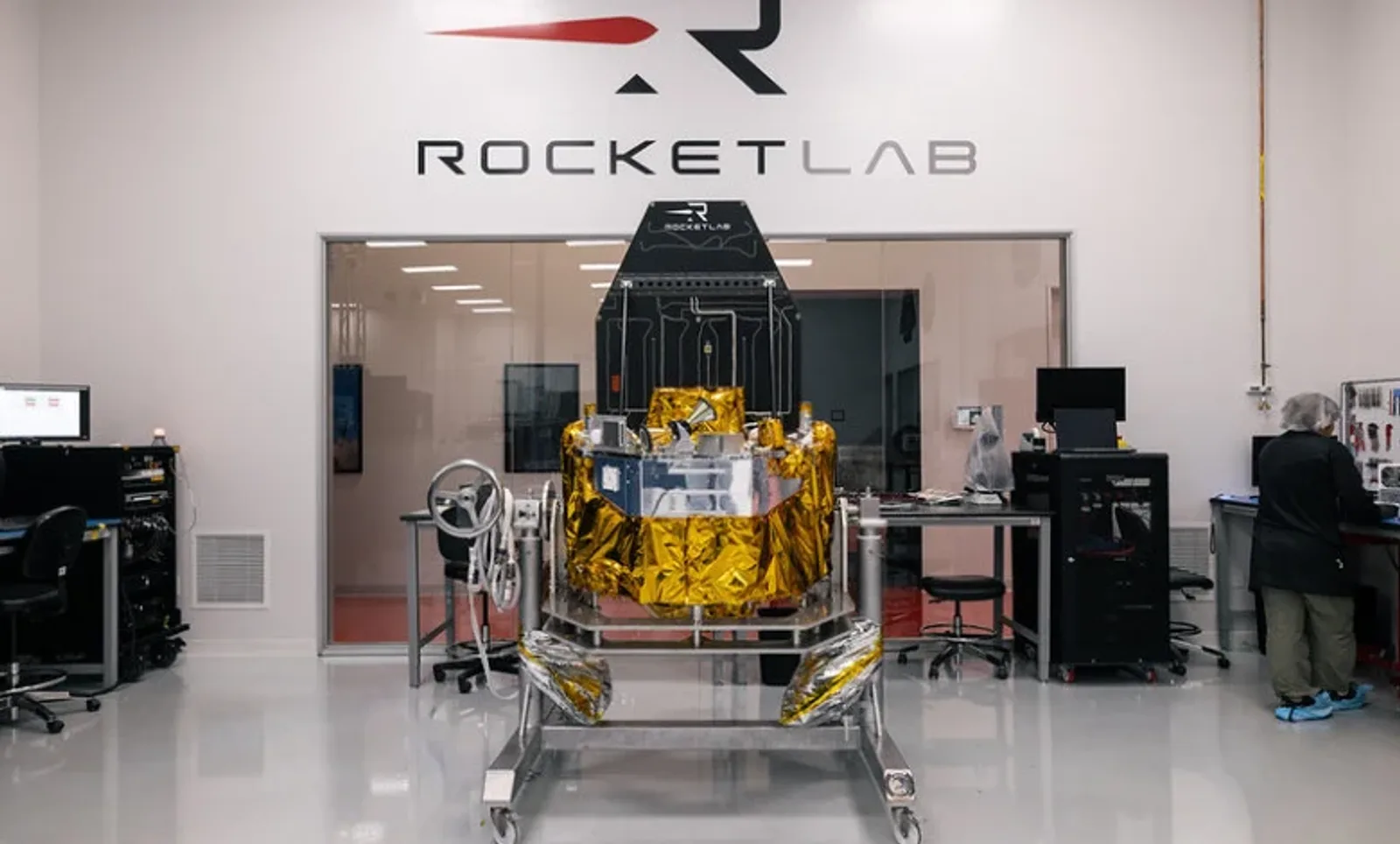 Satellit von Rocket Lab auf einer Montagevorrichtung in einer Fertigungshalle mit einem Mitarbeiter in Schutzkleidung