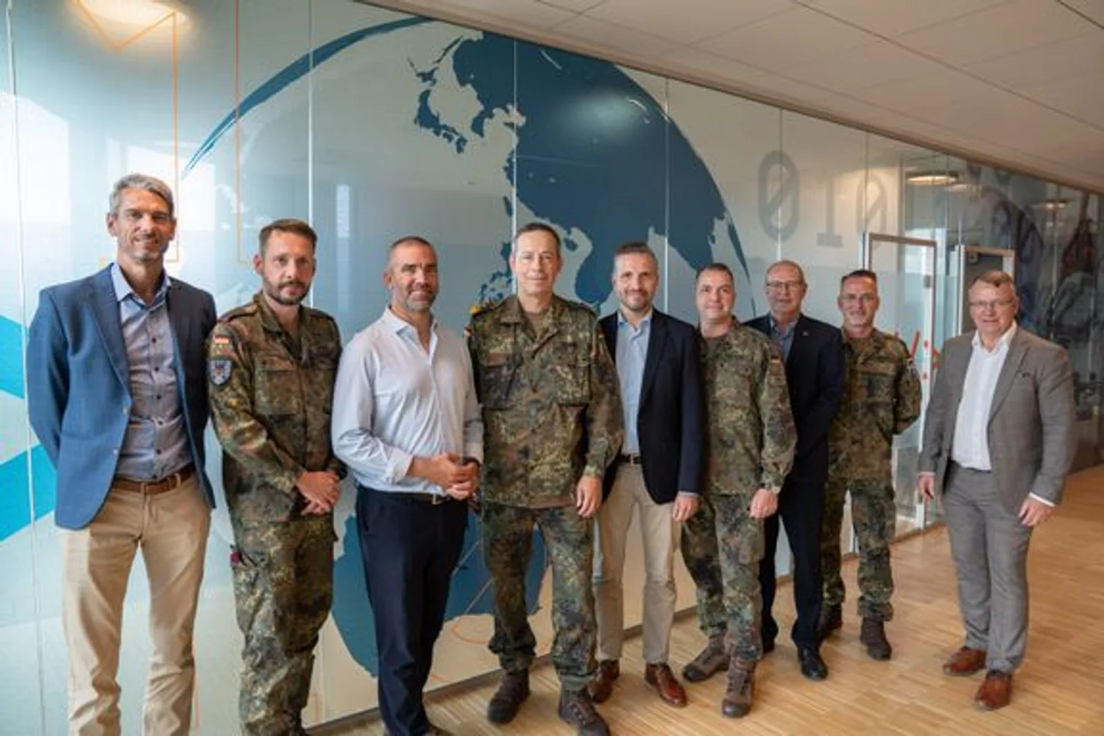 Generalleutnant Alfons Mais und eine Delegation der Bundeswehr posieren mit zivilen Vertretern vor einer Weltkarte