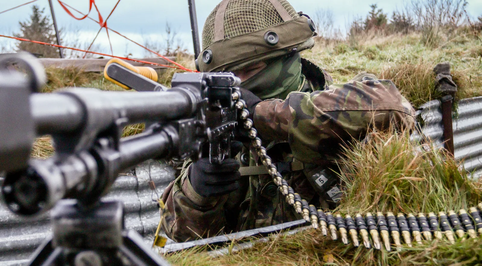 Soldat in Flecktarn zielt aus einer befestigten Stellung mit einem auf Lafette montierten Maschinengewehr samt Duellsimulationssystem
