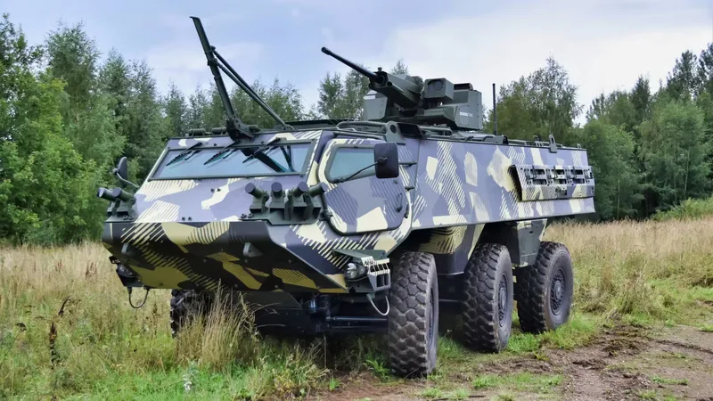 Radpanzer Patria 6x6 mit Cockerill CLWS Waffenstation und geometrischer Tarnung auf einer Freifläche vor einem Wald