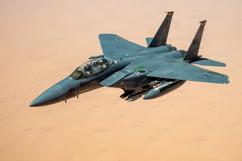 US Air Force F-15E Strike Eagle mit externen Tanks und Lenkwaffen im Flug über einer Wüstenlandschaft