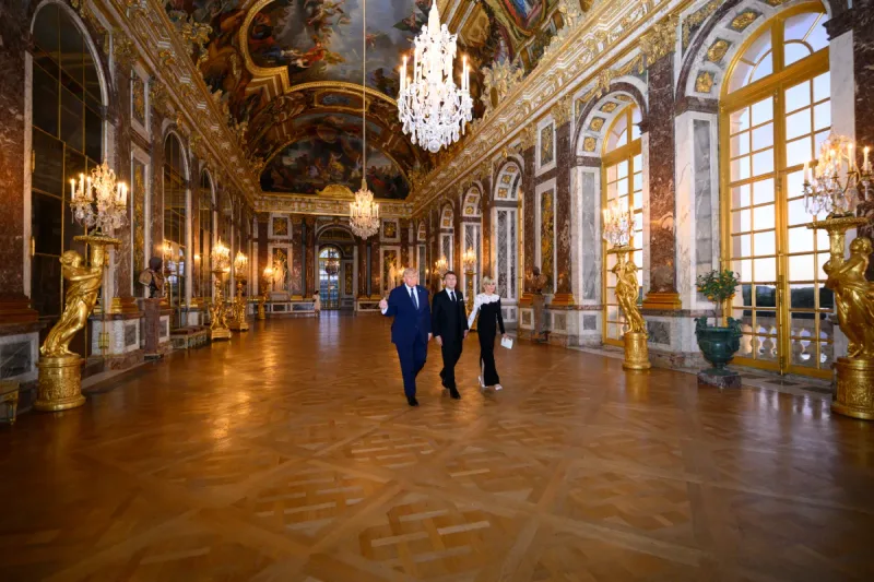 Donald Trump, Emmanuel Macron und Brigitte Macron gehen gemeinsam durch den Spiegelsaal im Schloss Versailles