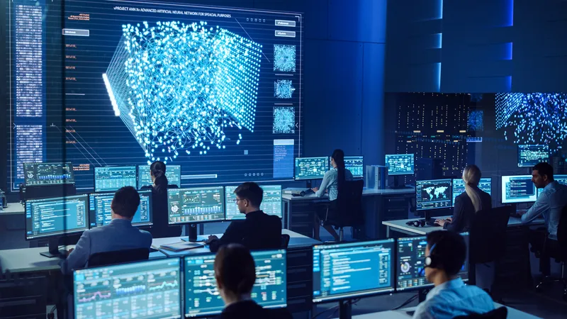 Mitarbeiter in einem Kontrollzentrum überwachen Datenströme vor einer Videowand mit der Visualisierung eines neuronalen Netzwerks