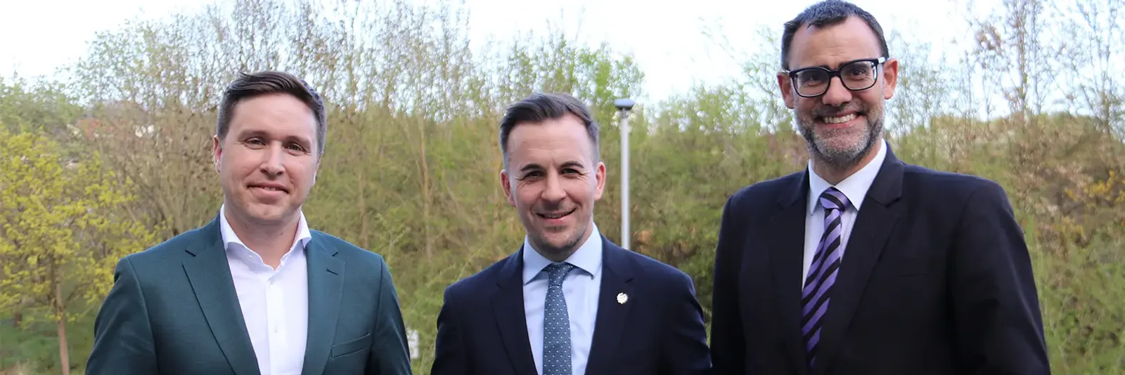 Michael Ernst, Christian Limbacher und Ben Edelhäusser von Elbit Systems Deutschland in Anzügen vor einer Baumkulisse