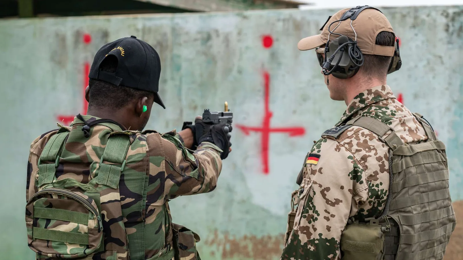 Ghana: Bundeswehr-Soldat in Drei-Farben-Tarndruck überwacht einen Partnersoldaten beim Schießen mit einer Pistole auf rote Zielmarkierungen