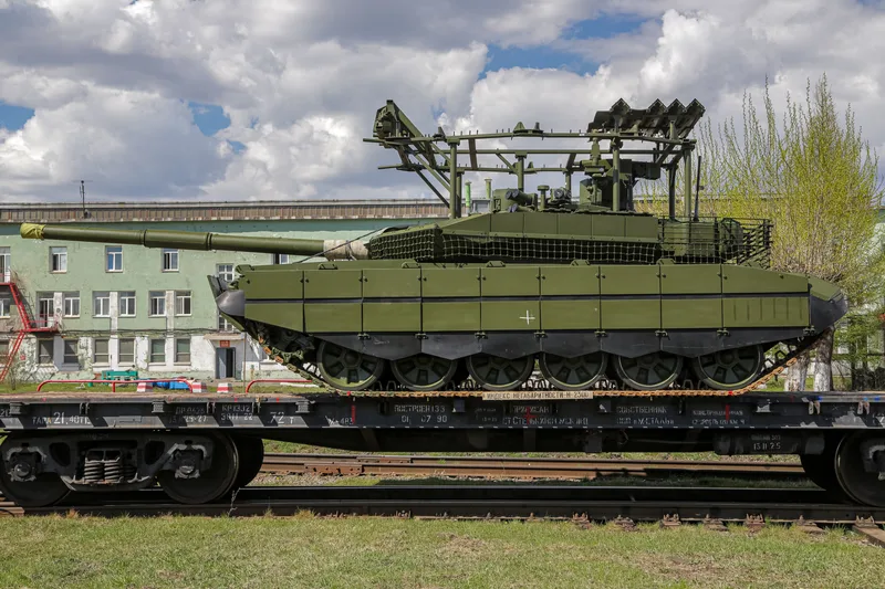 Ein T-90M-Kampfpanzer mit dem neuesten bekannten Typ von Dachschutz wird im Mai 2026 im UVZ-Werk auf einen Eisenbahnwaggon verladen.