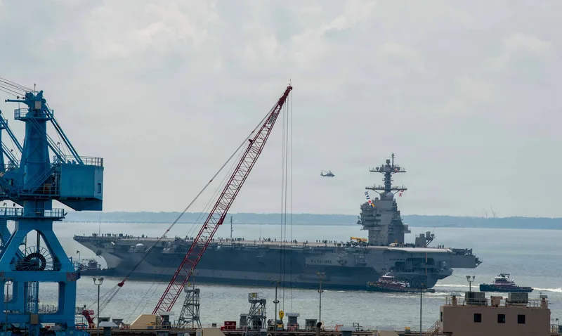 Flugzeugträger USS John F. Kennedy (CVN-79) der US Navy bei Manövern mit Schleppern in einer Werft mit Kränen und Hubschrauber