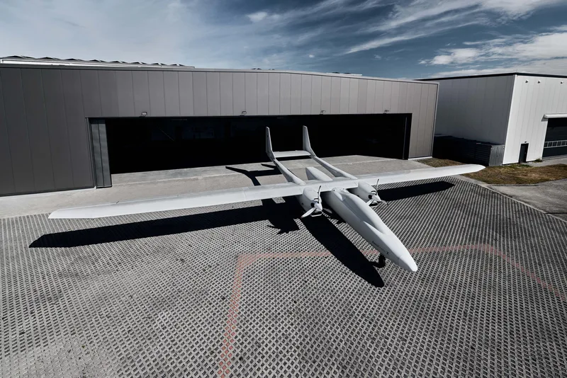Zweimotorige Drohne AeroForce X von Aerodata mit Doppelrumpf-Bauweise auf einem gepflasterten Flugfeld vor einer Halle