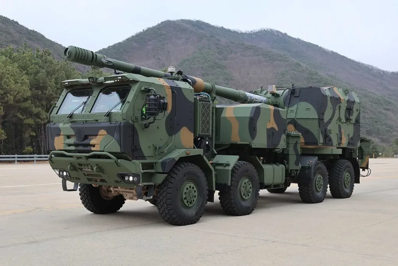 Radhaubitze K9MH von Hanwha Aerospace im dreifarbigen Tarnmuster auf einer Freifläche vor einer bewaldeten Bergkulisse