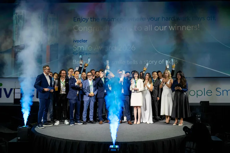 Preisträger posieren mit Trophäen auf der Bühne des Ivoclar Smile Award vor einer Firmenleinwand mit blauen Raucheffekten