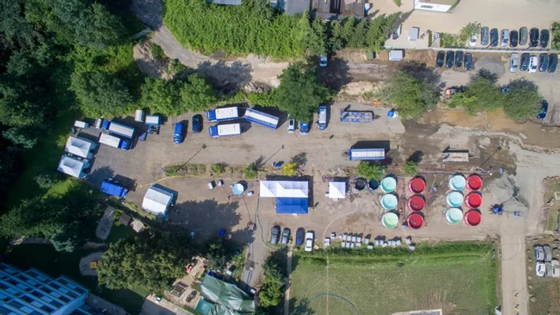 THW: Luftaufnahme einer THW-Station zur Trinkwasseraufbereitung mit blauen Einsatzfahrzeugen, Zelten und kreisförmigen Wasserbecken