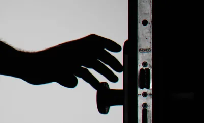 Wohnungseinbruch: Hand greift nach dem Knauf einer geöffneten Tür mit steckendem Schlüssel und sichtbarem NEMEF-Logo auf dem Einsteckschloss
