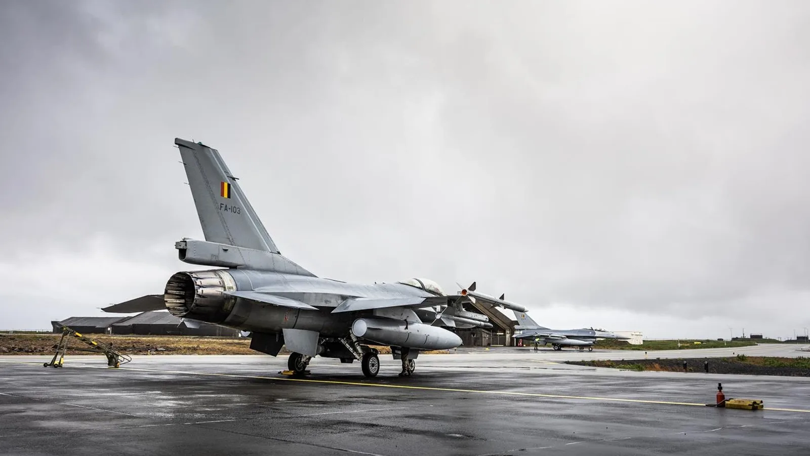Arctic Sentry – Belgien übernimmt Luftverteidigung. Zwei F-16 Kampfflugzeuge der belgischen Luftstreitkräfte auf einem nassen Rollfeld, im Vordergrund die Heckansicht der FA-103