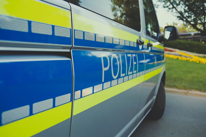 Clankriminalität: Blau-silbernes Polizeifahrzeug mit neongelben Warnmarkierungen und reflektierendem Schriftzug Polizei am Straßenrand vor einer Grünanlage