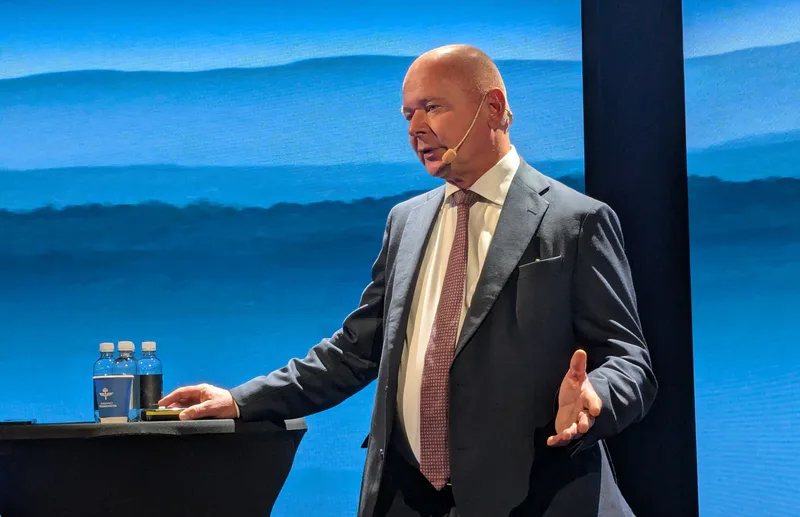 Saab-CEO Micael Johansson spricht während einer Präsentation an einem Stehtisch vor einer blauen Hintergrundleinwand
