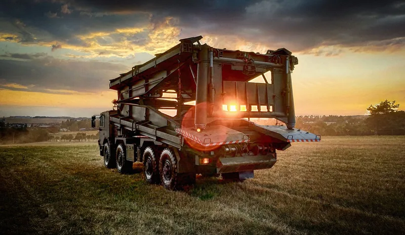 Ein Brückenlegefahrzeuge des Typs AM-50 EX steht auf einem geländegängigen 8x8-Fahrgestell im Abendlicht.