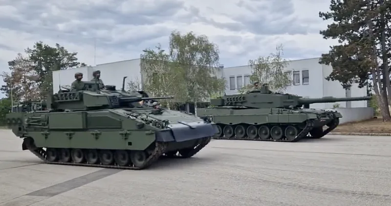 Bundesheer: Schützenpanzer Ulan und Kampfpanzer Leopard 2A4 mit Besatzung in den Luken fahren nebeneinander auf einer asphaltierten Fläche