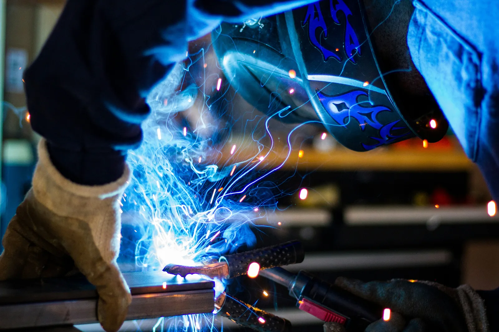 Industrie: Arbeiter in einer Werkstatt beim Schweißen von Metallprofilen mit Schutzhelm und Handschuhen