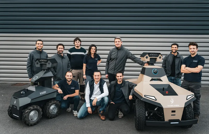 Robo: Mitarbeiter von Running Brains Robotics posieren vor einer Hallenwand mit den unbemannten Bodenfahrzeugen GR100 und GR200